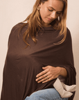 A woman wearing a dark brown shawl or poncho draped over her shoulders, paired with blue jeans and a light beige cardigan, set against a plain beige background.