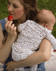 Woman holding a baby in a strawberry outfit while eating a strawberry outdoors. @marygraceking