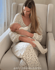 Woman in a strawberry outfit holding a baby in a beige armchair. @Bellerasmussenn