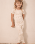 Girl wearing cream-colored short sleeve top and pants pajama set with small floral pattern.