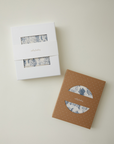 Two packaged fabric sets with blue toile print, one in white box and one in brown box with white polka dots, labeled "jollybaby".