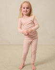 Young girl wearing a light pink long-sleeve ribbed top and matching ribbed pants standing barefoot.