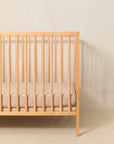 A simple wood crib styled with a Solly Baby Crib Sheet in the Cream Floral print featuring petite cream buds gently scattered atop a soft taupe brown base.