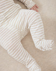 A close-up of a baby wearing cream and beige striped footed pajamas, lying on a soft beige blanket.