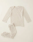 A two-piece baby pajama set featuring a long-sleeve top and matching footed pants, both with thin horizontal beige stripes on an off-white base, laid flat on a light cream background.
