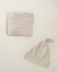 Beige and white striped baby blanket and knotted hat set on a cream background.
