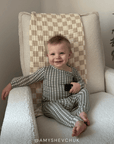 Child wearing a green and white gingham sleep set sitting on a cushioned chair with text overlay. Features the instagram handle @amyshevhuk
