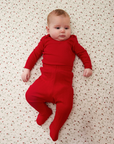 Baby wearing a red pointelle outfit lying on a strawberry patterned surface