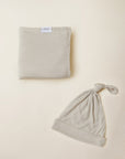 Beige baby blanket with label and matching beige baby knotted hat on light background.