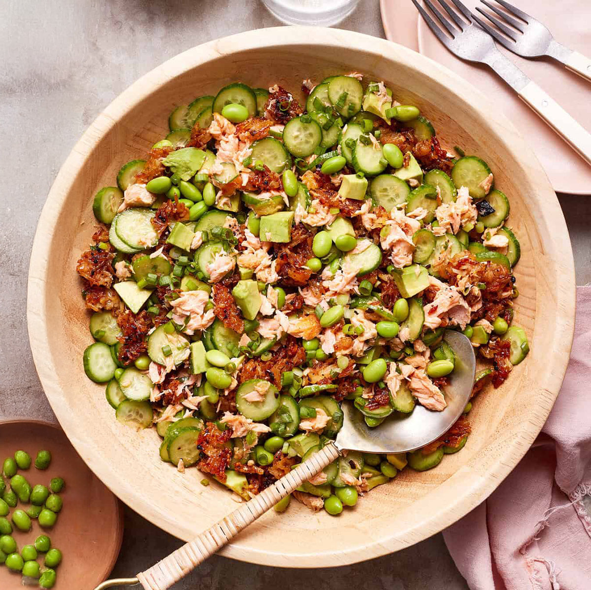 Salad with cucumber, edamame, salmon, crispy rice, and diced avocado in a wooden bowl with a spoon