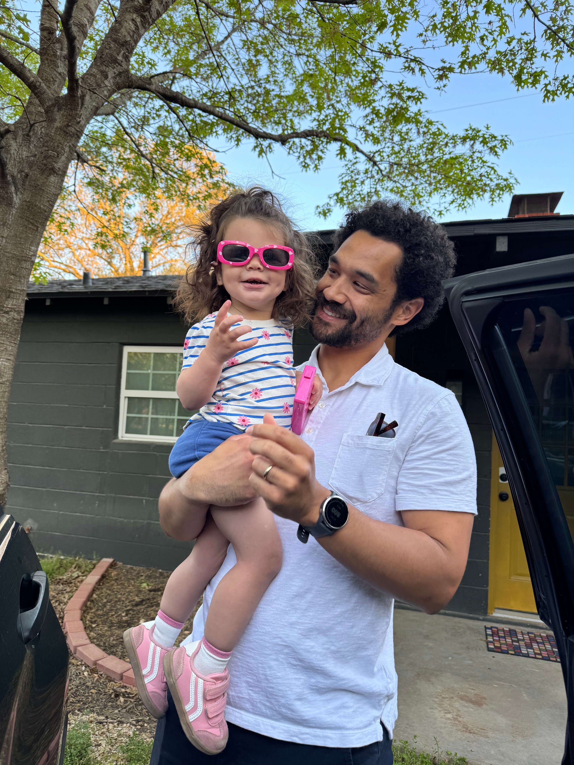 Father standing outside with house in the background while holding his daughter and smiling
