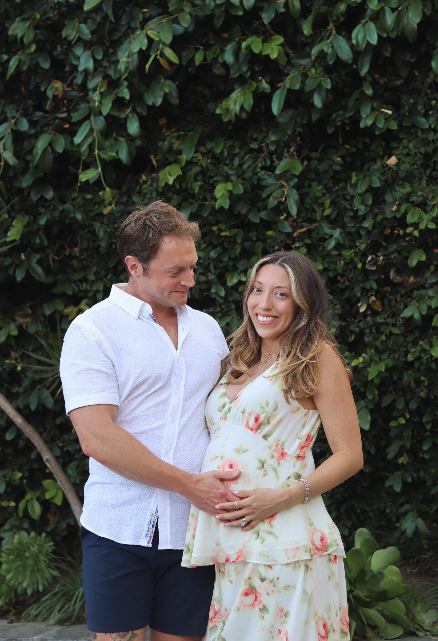 Pregnant woman standing beside husband both holding her belly and smiling