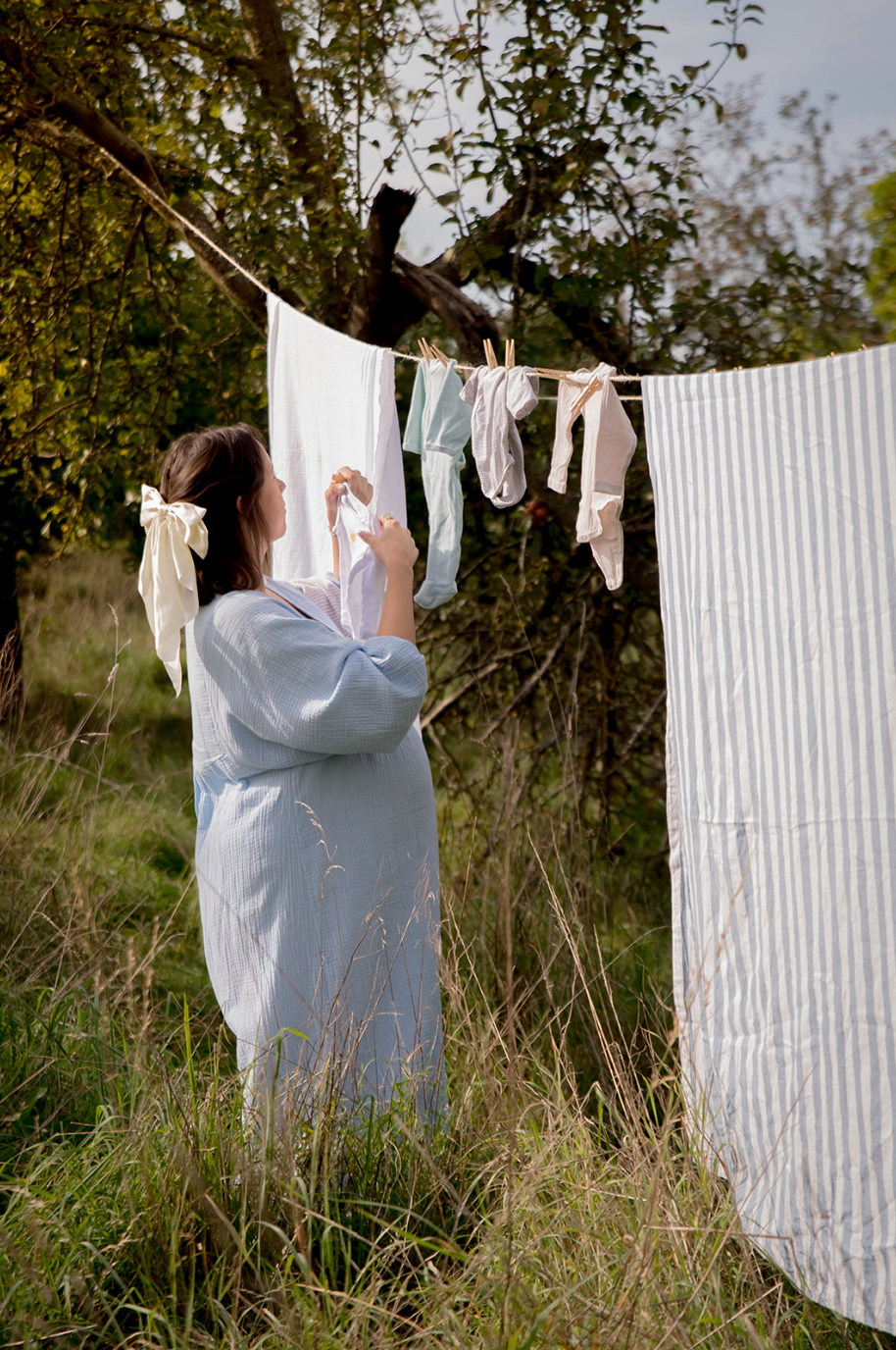 Pregnant mom hang-drying baby laundry on clothesline outside