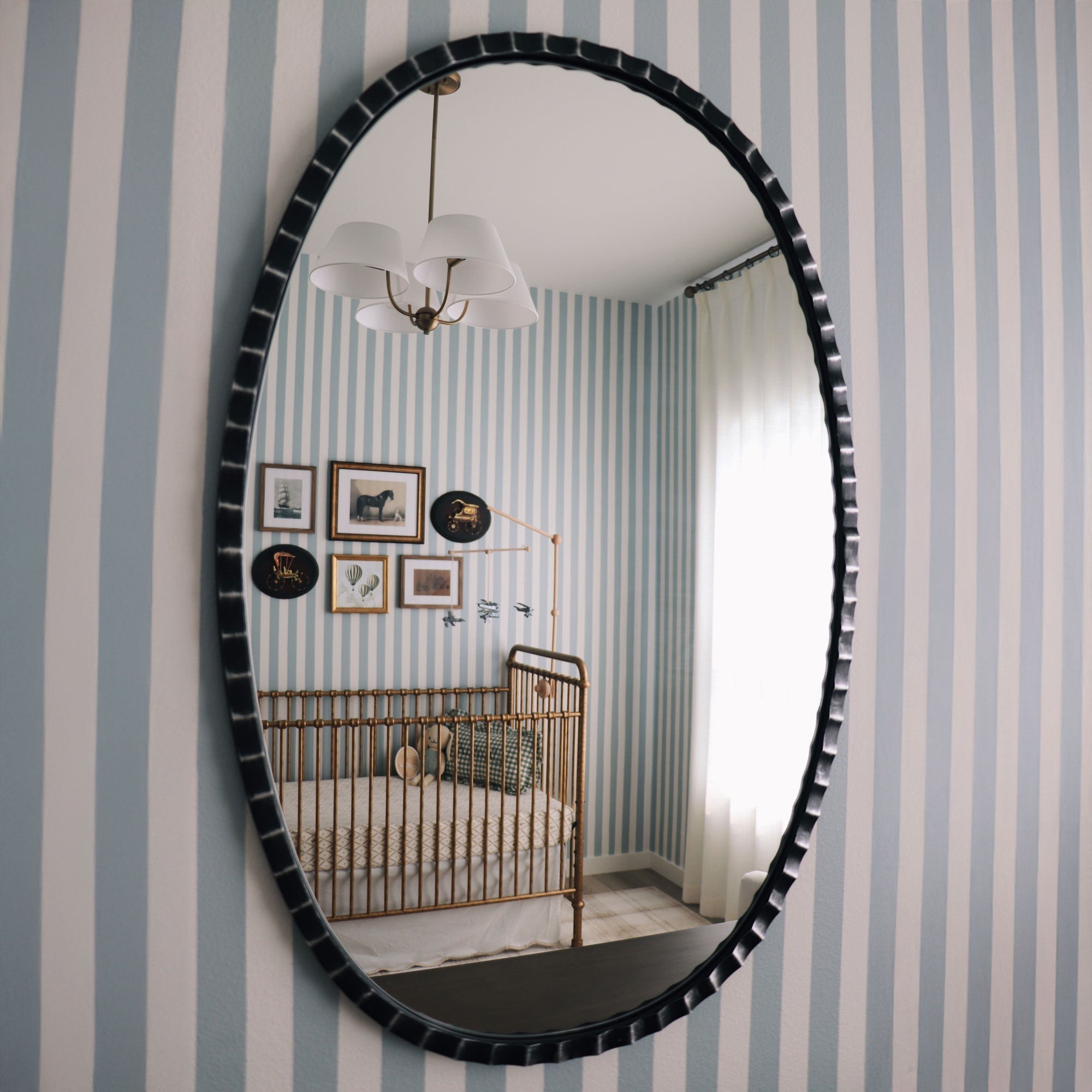Vintage baby nursery with brass crib and striped walls reflected in mirror.