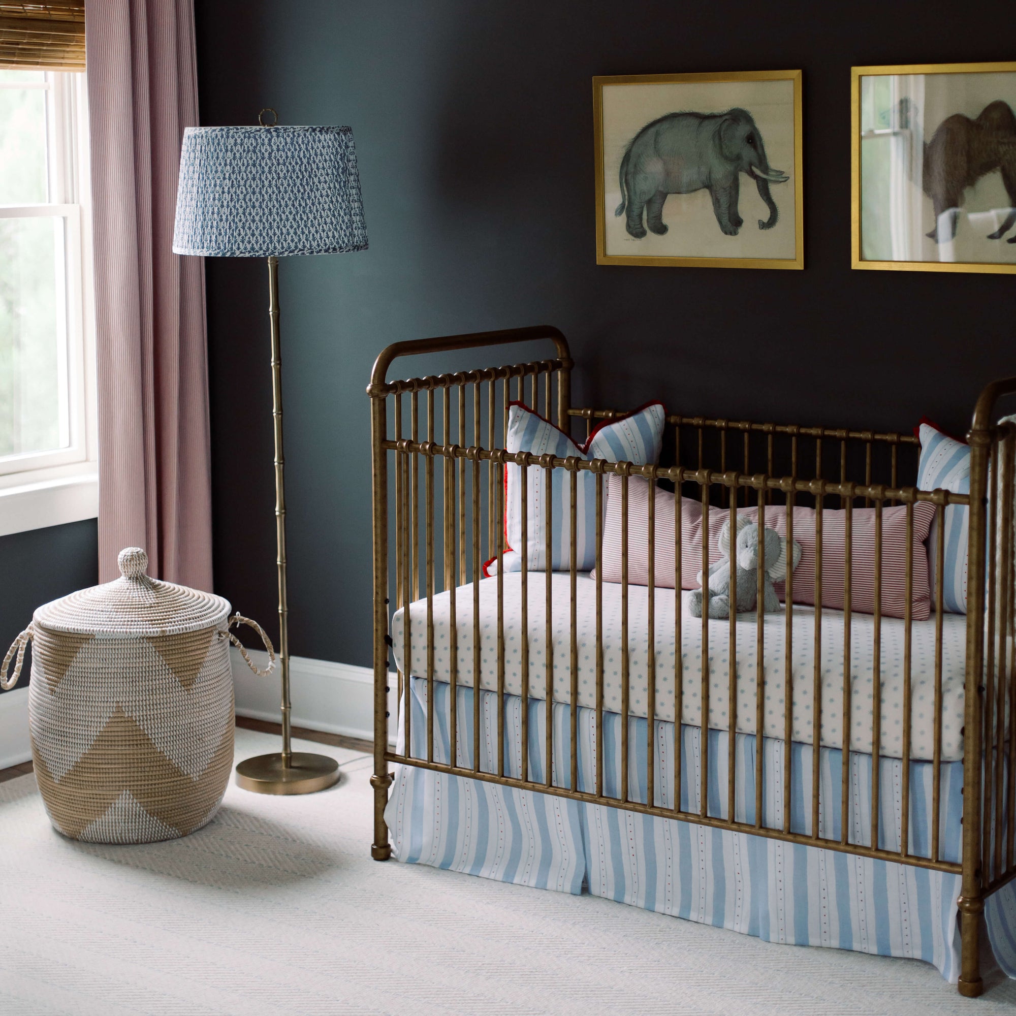 Classic baby boy's nursery with dark, blue-gray walls, a brass antique crib, and animal paintings hanging on the wall