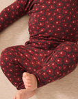A close-up of a baby wearing a dark red and black floral patterned long-sleeve pajama set, lying on a light beige textured floor.