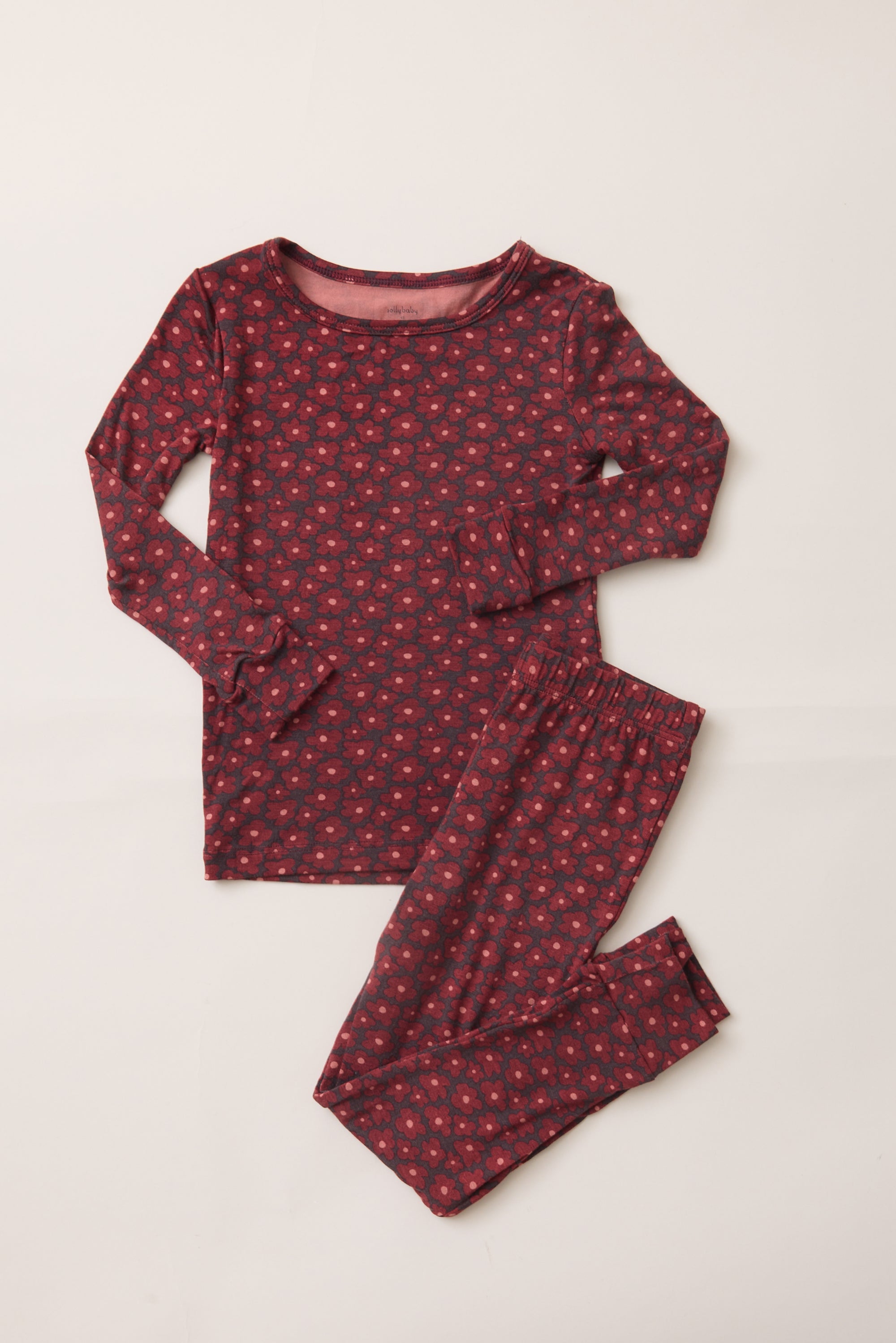A two-piece long-sleeve pajama set laid flat on a light beige background. The set features a dark red top and matching pants with a small, repeating red and pink floral pattern.