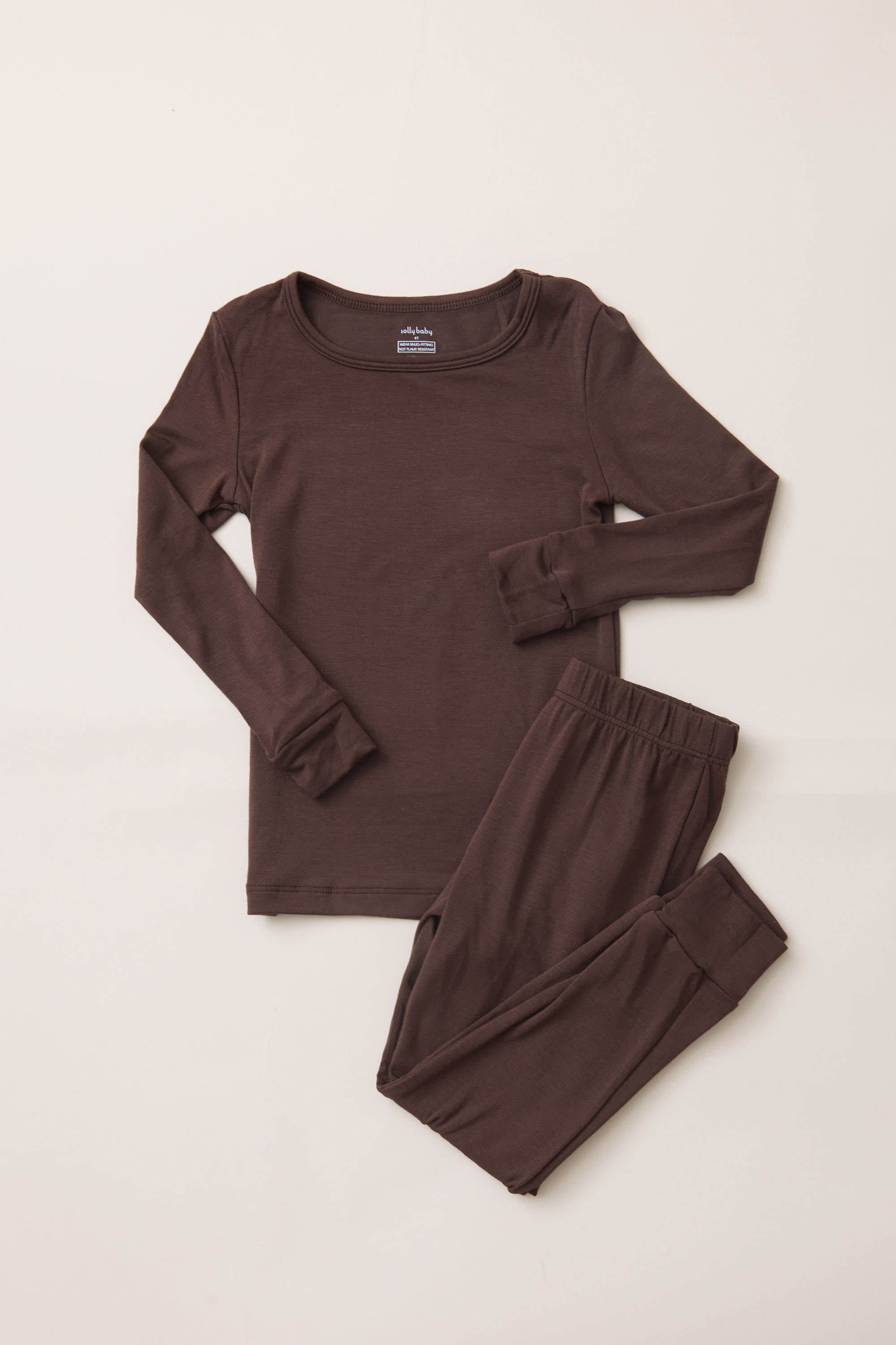 A two-piece children's pajama set in dark brown, featuring a long-sleeve top with rolled cuffs and matching pants with elastic waistband and leg cuffs, laid flat on a light beige background.