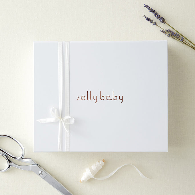 White Solly Baby gift box with white ribbon, scissors, ribbon spool, and sprigs of lavender on cream background