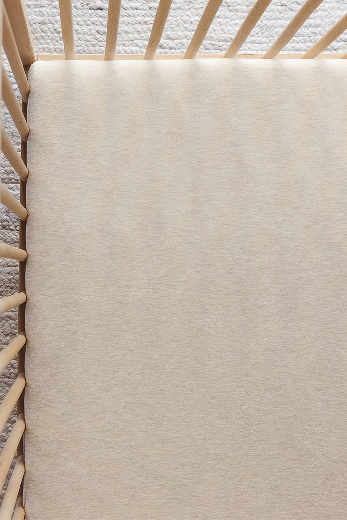 Beige fitted crib sheet on a wooden crib mattress with vertical slats and carpeted flooring underneath.