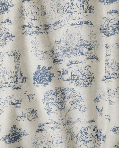 A close-up of a fabric with a classic blue toile de Jouy pattern on an off-white background, showing detailed illustrations of rural scenes, trees, and animals.