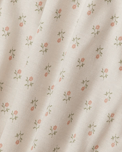 Close-up of a cream-colored fabric with a delicate, repeating floral pattern of small pink flowers and green stems.