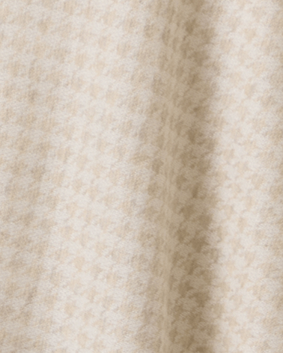 A close-up of a soft, textured fabric with a fine houndstooth pattern in cream and light beige, showing a vertical fold.
