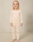 Toddler wearing beige ribbed long sleeve top and matching ribbed pants, standing barefoot on beige carpet.