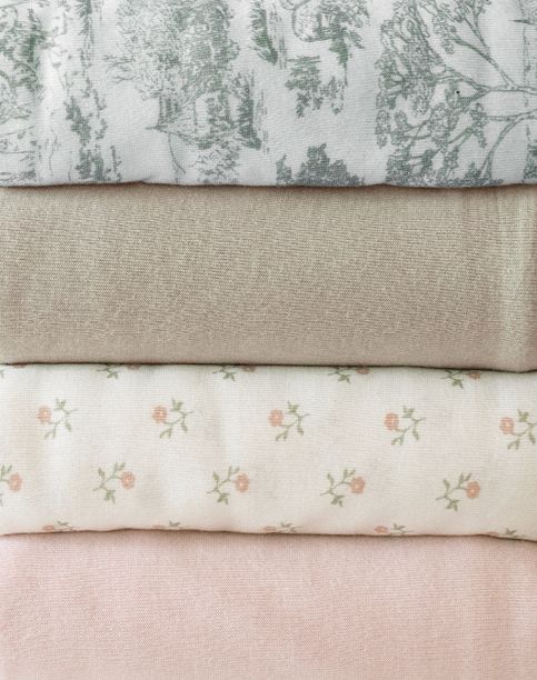 Stack of four folded fabrics featuring green toile print, solid beige, white with small pink flowers, and solid pink colors.