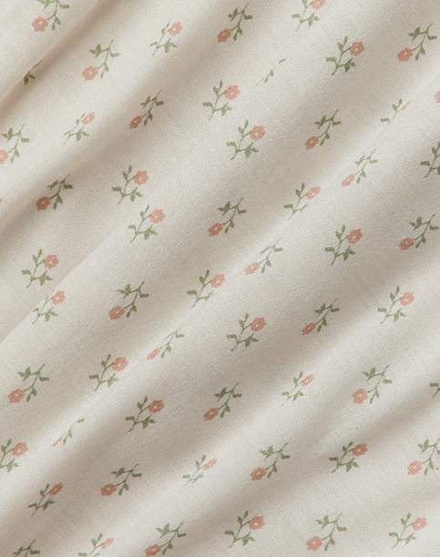 Cream fabric with small pink floral pattern and green stems, displaying gentle folds.