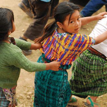 Colorful woven traditional blouse with blue and yellow patterns worn by a child playing outside.