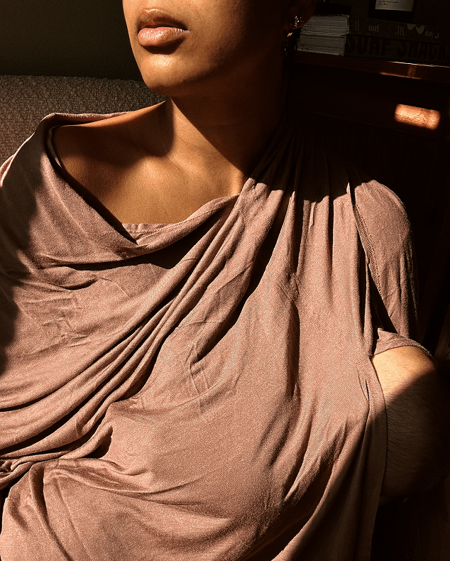 Woman wearing a loose-fitting beige draped top with an off-shoulder style in warm natural light.
