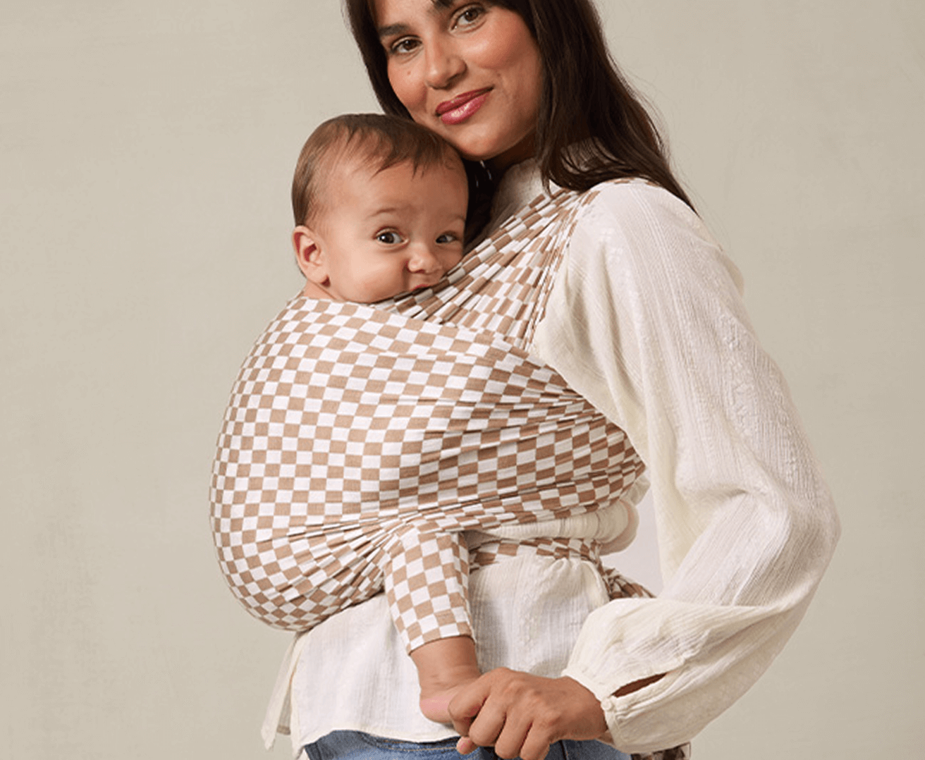 Woman holding a baby in a checkered wrap against a plain background