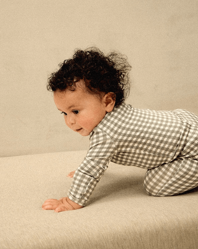 Baby in a green gingham outfit crawling on a beige surface