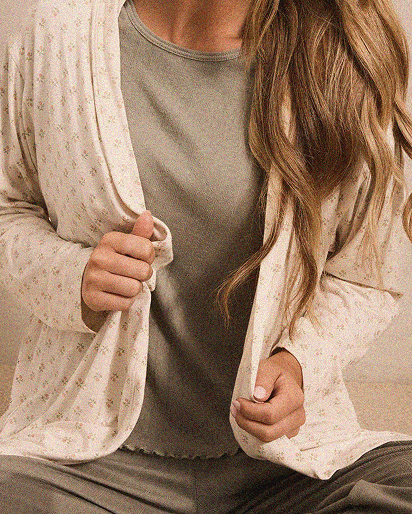 Woman wearing a light beige cardigan with small floral print over a sleeveless grey top and gray pants.