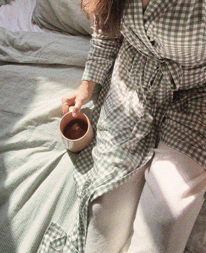 Long green and white checkered robe with a waist tie worn over white pants, with a pink cup held in hand.