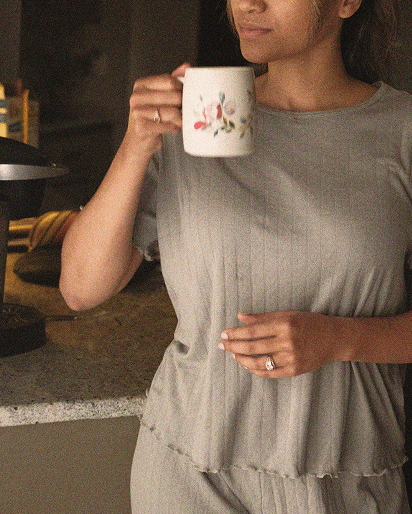 Woman in a light gray ribbed short sleeve top and pants holding a white ceramic mug with floral design.