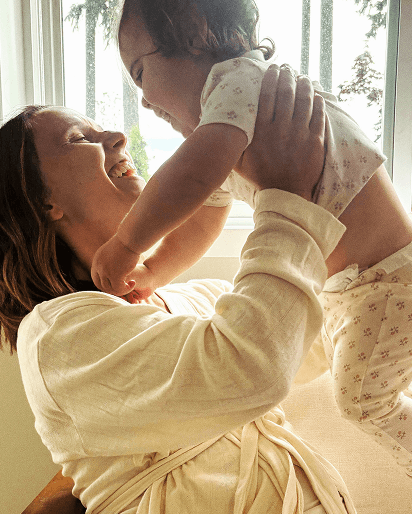 Woman in a cream-colored robe holding a baby dressed in white pajamas with a small floral pattern.