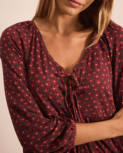 A close-up of a woman wearing a long-sleeve dark pink and brown top with a tie neckline.