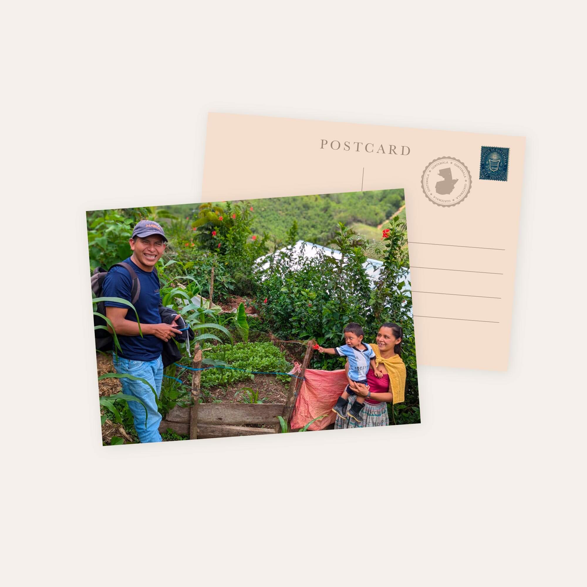 Postcard with color photo of smiling man in blue shirt and cap, woman in traditional skirt holding a child in garden setting