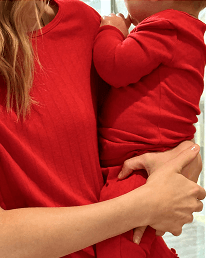 A close-up lifestyle shot of a woman in a red long-sleeve top holding a child dressed in a matching red outfit.