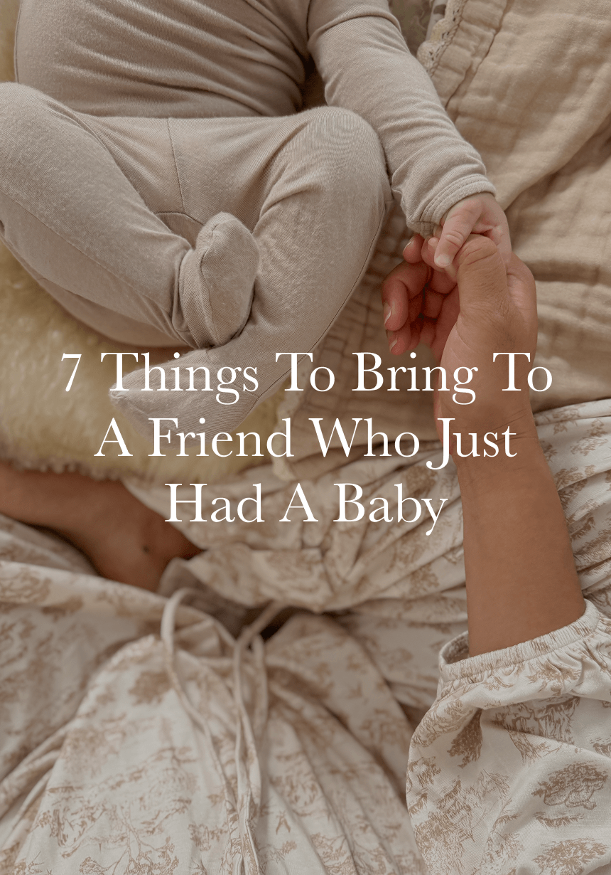 Baby in beige footed onesie holding adult's hand, adult wearing cream and beige patterned dress on soft blankets.