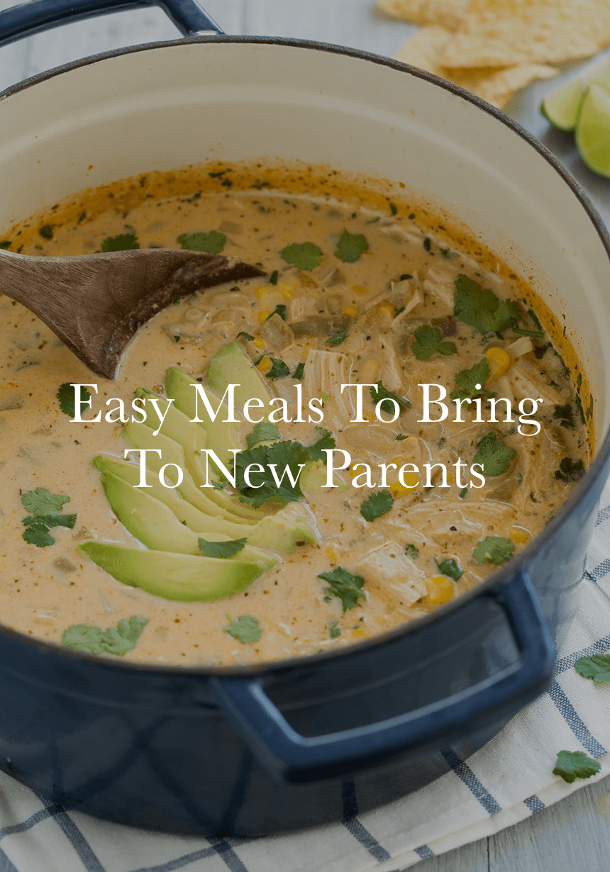 Blue pot of creamy chicken and corn soup garnished with avocado slices and cilantro, wooden spoon inside.