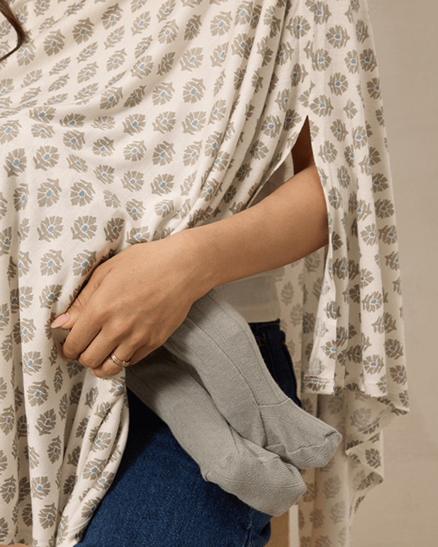 Person wearing a floral-patterned dress holding a gray garment against a neutral background