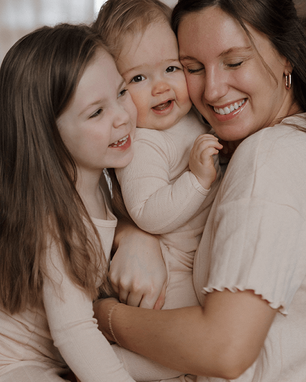 Woman holding a baby and a young girl, all smiling.