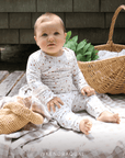 Baby sitting on a blanket with a basket and plant in the background, wearing a strawberry patterned outfit. @kendraqual