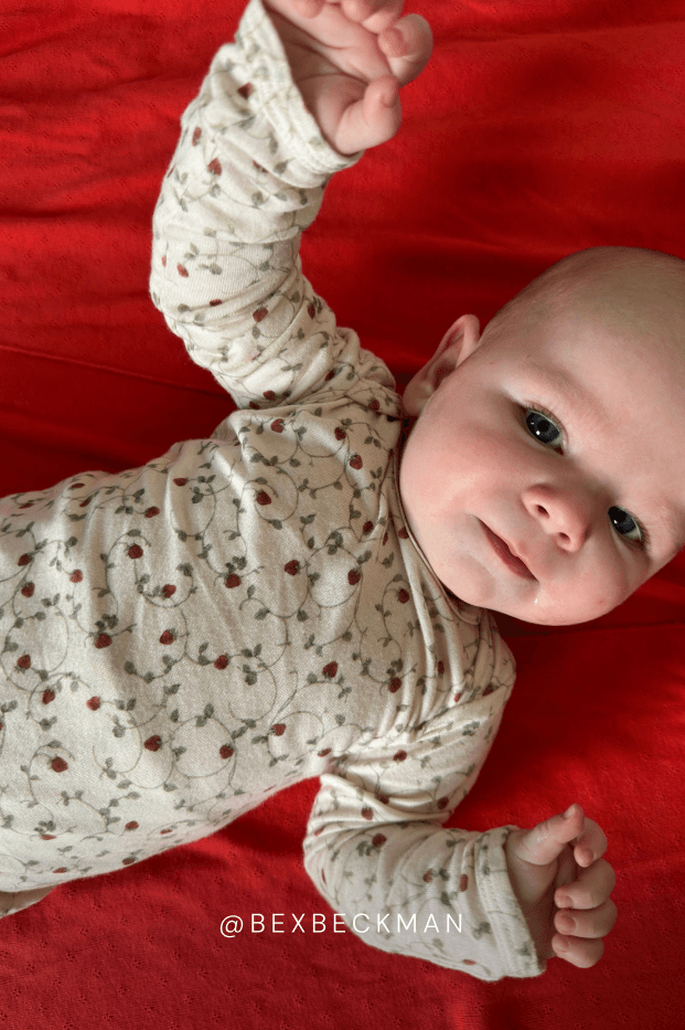 Baby wearing a strawberry pajama set on a red blanket @bexbeckman