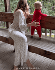 Woman in a strawberry outfit sitting on a wooden bench with a child in red outfit, both looking out over a railing. @marybethaker