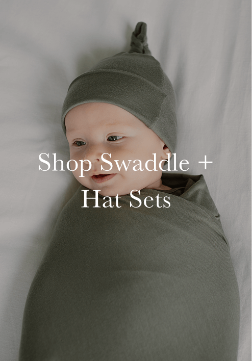 Baby swaddled and wearing matching olive green hat with top knot, lying on white fabric background.