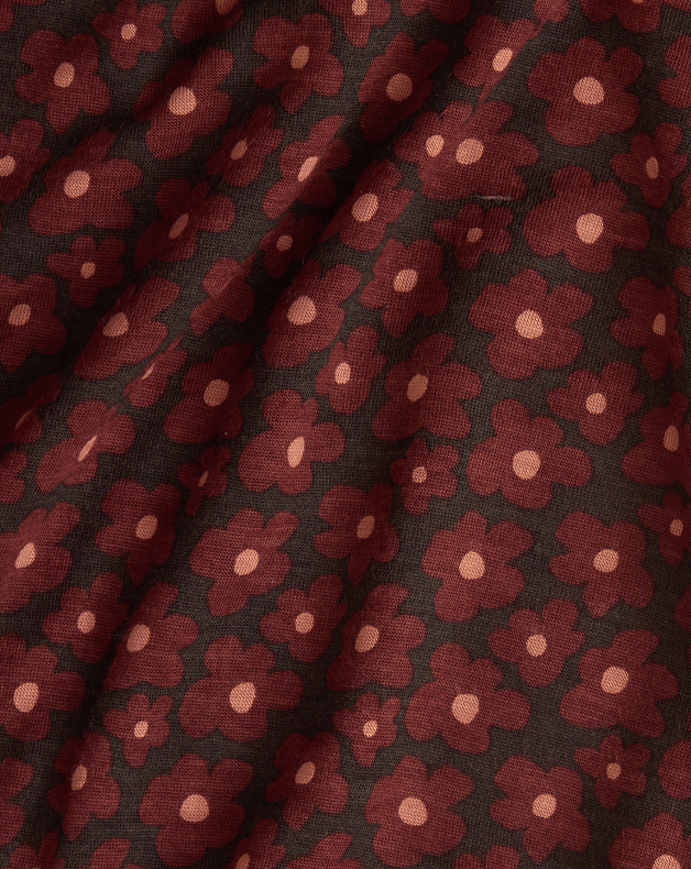 A close-up of a draped fabric with an allover floral pattern. The fabric features dark reddish-brown flowers with light pink centers on a dark brown background.